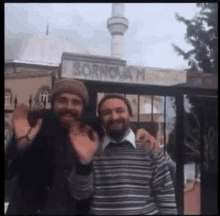 two men are posing for a picture in front of a building with a mosque in the background .