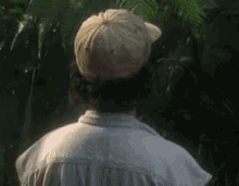 a man wearing a hat and a white shirt is standing in the woods .