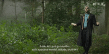 a man in a trench coat is standing in the woods holding a book .