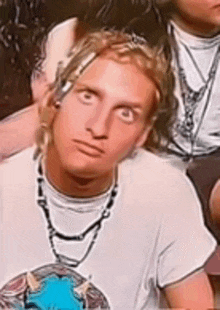 a young man with dreadlocks is wearing a white shirt and a necklace .