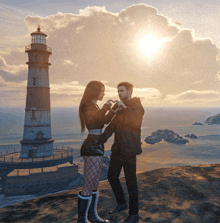 a man and a woman are standing in front of a lighthouse and making a heart shape with their hands