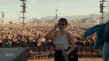 a woman wearing sunglasses stands in front of a crowd at a music festival with the word coachella on the bottom