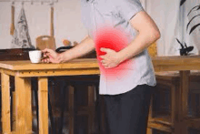 a man is holding his stomach in pain while sitting at a table .