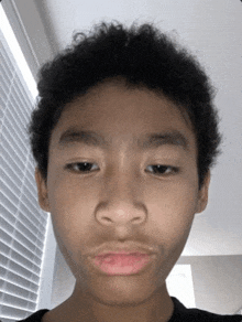 a young boy with curly hair is making a funny face in front of a window