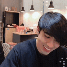 a young man is smiling while sitting at a table in a room with a kitchen in the background .