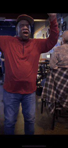 a man wearing a red shirt and a hat is standing with his arms outstretched