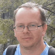 a man wearing glasses and a backpack is standing in front of trees .