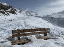 a wooden bench sits in the snow with a mountain in the background and a sign on it