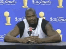 a man is sitting at a table with a microphone in front of a blue wall that says the finals