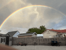 a double rainbow is visible over a backyard with bikes and a wheelbarrow in the foreground