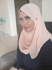 a woman wearing a pink hijab and a black shirt is sitting on a couch