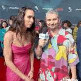 a man in a colorful shirt is talking to a woman in a pink dress on the red carpet .