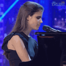 a woman is singing into a microphone while playing a piano in front of a sign that says " get a talent "