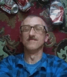 a man wearing glasses and a blue shirt is laying on a carpet next to a pile of cans .