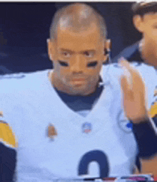 a football player wearing a white jersey with the number 4 on it is sitting on the sidelines .