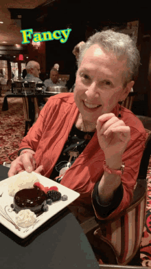 a woman is sitting at a table with a plate of dessert in front of a sign that says fancy