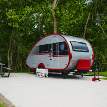 a silver and red camper is parked in a parking lot with trees in the background