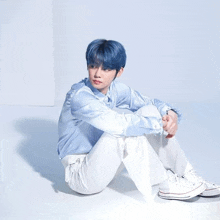 a boy with blue hair is sitting on the floor wearing white pants and converse shoes .