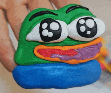 a person is holding a green and blue frog with big eyes