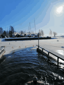 a person is swimming in a frozen lake with a dock in the background