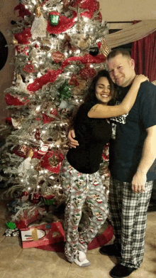 a man and woman pose in front of a christmas tree with the man wearing a shirt that says ' everlast '