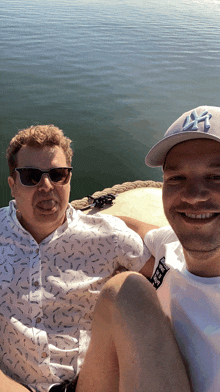 a man wearing a ny hat sits next to another man wearing sunglasses