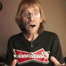 a man wearing glasses and a black shirt with a budweiser logo on it is making a funny face .