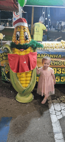 a little girl stands in front of a statue of a corn on the cob