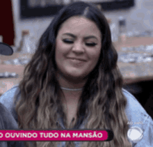 a woman with long hair is smiling in front of a sign that says " ouvindo tudo na mansão "