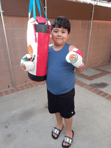 a young boy wearing pink sandals holds a punching bag and boxing gloves