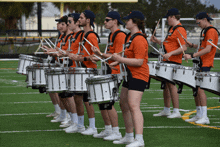 a group of people playing drums with one wearing an orange shirt that says ' army ' on it