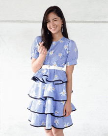 a woman wearing a blue striped dress with white daisies on it is making a heart shape with her hand