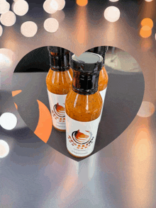 three bottles of hot sauce with a white label on a heart shaped background