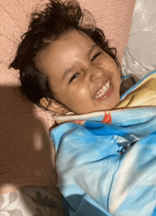 a little girl wrapped in a blue and yellow blanket smiles for the camera