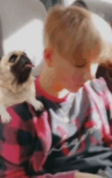 a young boy is sitting on a couch holding a pug dog .