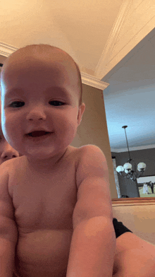 a baby without a shirt is looking at the camera and smiling