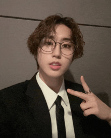 a young man wearing glasses and a suit is giving the peace sign