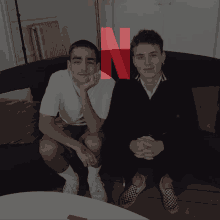 two men sitting on a couch with a red n on the bottom