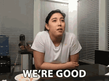 a woman sitting at a table with a bowl of food and the words " we 're good " above her