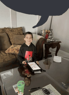 a young boy sits at a table with a tablet and a speech bubble above him