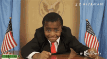 a boy in a suit and tie is sitting at a desk with american flags behind him and the words soulpancake on the bottom