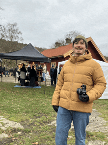 a man in a yellow jacket holds a camera in front of a tent