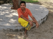 a man in an orange shirt sits on a cement curb