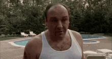 a bald man in a white tank top is standing in front of a pool