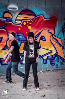 a man and a woman are standing in front of a wall with graffiti on it that says " a "