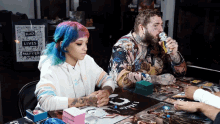 a man and a woman sit at a table with a sign that says black lives matter in the background