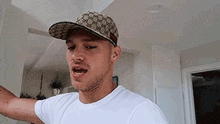 a man wearing a baseball cap and a white shirt is standing in a living room .