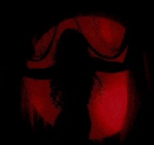 a silhouette of a woman with horns in a dark room with a red light behind her .