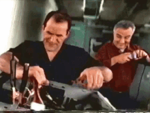 two men are working on a piece of equipment and one of them is smiling