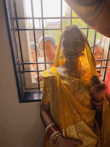 a woman in a yellow sari smiles while looking out of a window